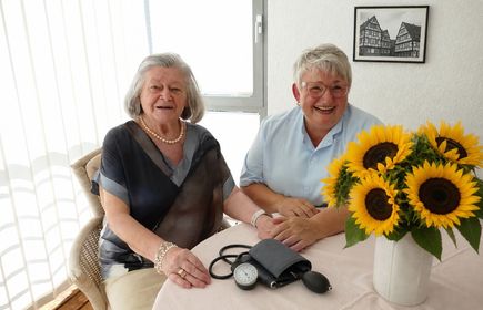 Zwei Frauen und ein Blutdruckmessgerät auf einem Tisch mit einer Vase mit Sonnenblumen