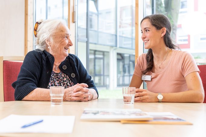 Ältere Frau und jüngere Frau lächelnd im Gespräch am Tisch