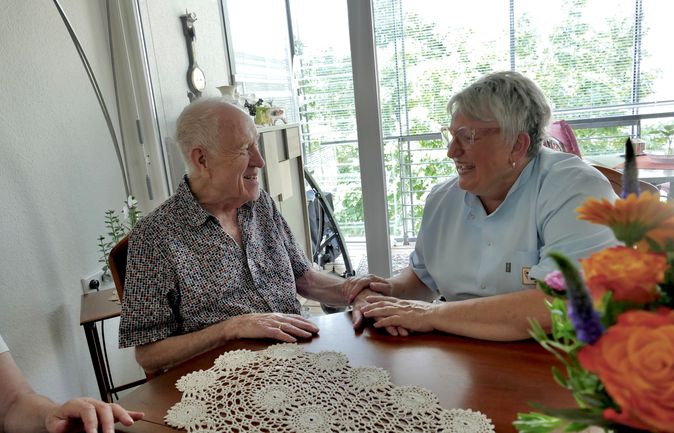 Ein älterer Herr und eine Pflegefachkraft an einem Tisch mit Blumen