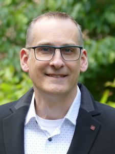 Porträt eines lächelnden Mannes mit Brille und Ohrpiercing