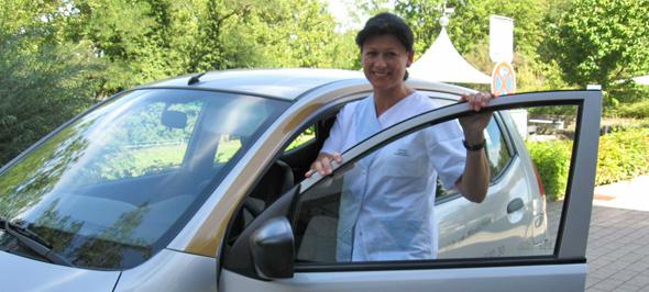 Person in weißer Arbeitskleidung steht an geöffneter Autotür